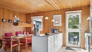 A modern kitchen with wooden walls, a dining area with red chairs, and a large window. - "Frode" - 400m from the sea by Interhome (Idestrup)