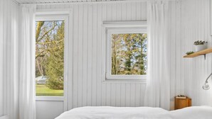 A bedroom with a large bed, two windows, a bedside table with a lamp, and a small shelf with a plant. - "Frode" - 400m from the sea by Interhome (Idestrup)