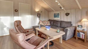 Ein gemütliches Wohnzimmer mit Holzboden, einer Couch, zwei Ledersesseln, einem Couchtisch und einem Bücherregal.