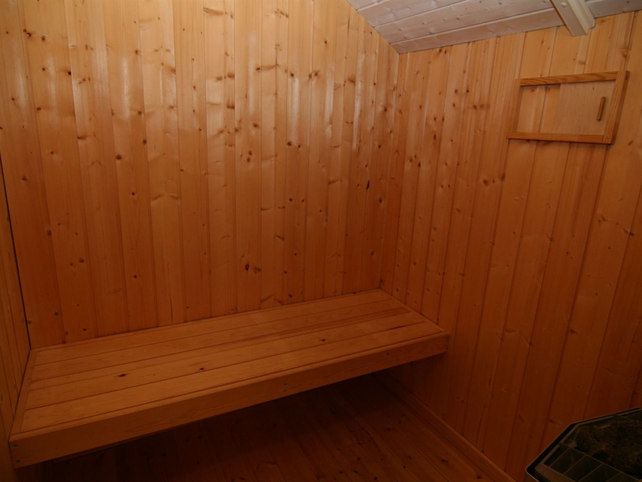 A wooden sauna room with a bench and a small wooden cabinet.