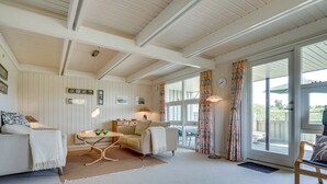 A cozy living room with a white sofa, a small table, and a lamp. There are curtains on the windows and a door leading outside. - "Inra" - 400m from the sea by Interhome (Fanø)