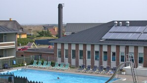 En swimmingpool med solstolar, ett trädäck och en byggnad med en fasad av tegel och solpaneler.