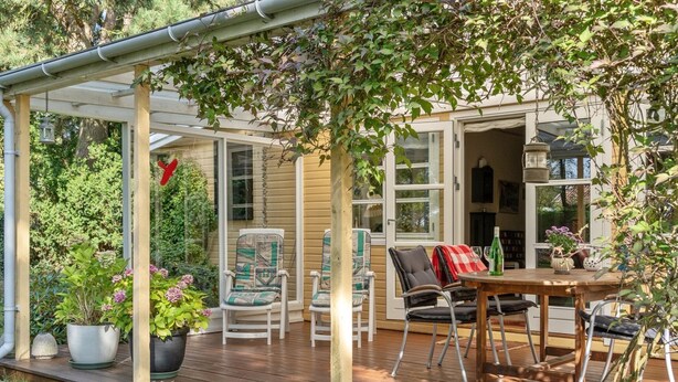 Eine überdachte Terrasse mit Sitzgelegenheiten, einem Tisch mit einer Flasche und Blumentöpfen.
