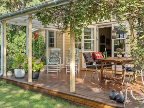 Une terrasse couverte avec des sièges d’extérieur, une table avec une bouteille et des plantes en pot.