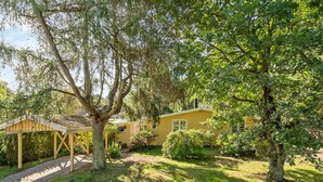 Ein gelbes Haus mit Veranda und einem Baum im Vordergrund.