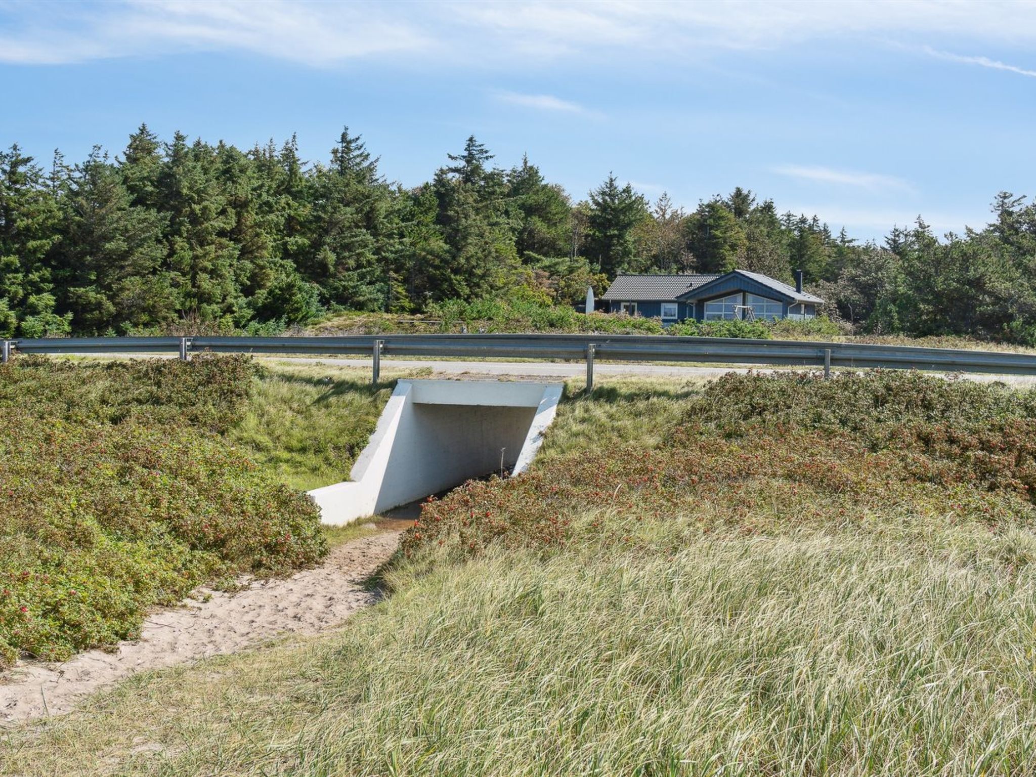 A coastal road with a concrete drainage structure and a house in the background.