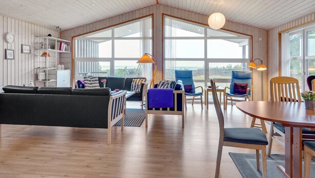 A spacious living area with a wooden ceiling, large windows, and a variety of seating options including a sofa, chairs, and a dining table.