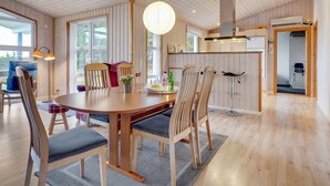 A spacious dining area with a wooden table and chairs, a hanging light fixture, and a view of the outdoors through large windows.