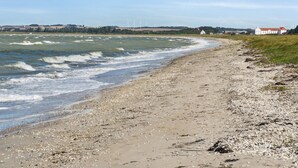 A coastal beach with a pebble shore, waves, and a distant view of wind turbines and buildings.