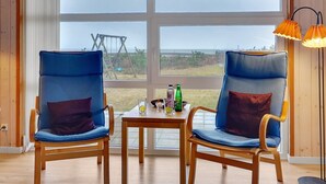 A room with two blue chairs, a small table with drinks, and a view of the outdoors through large windows.