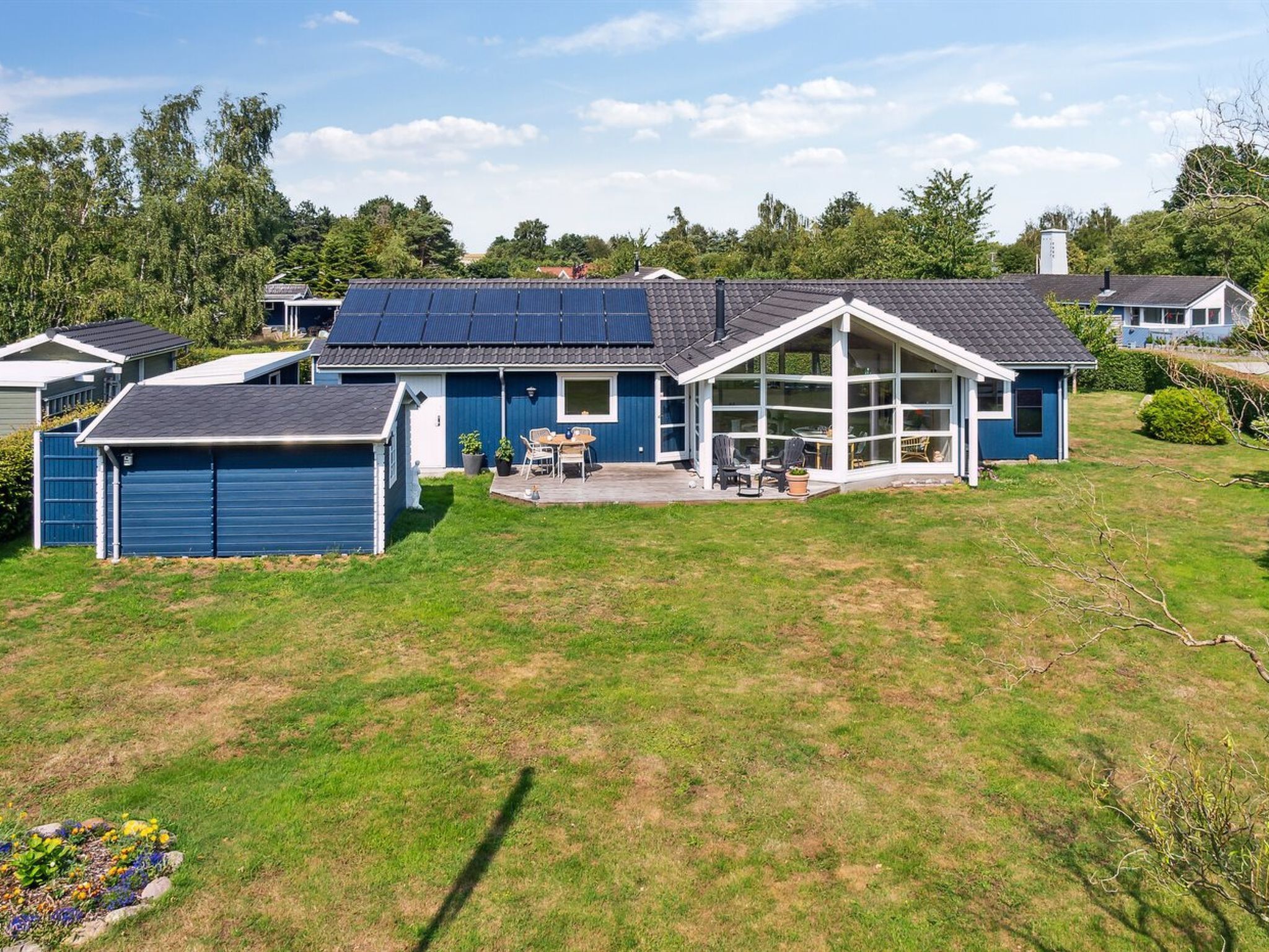 Ein modernes Haus mit großer Garage, überdachter Terrasse und Solaranlage auf dem Dach.