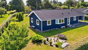 Een gelijkvloers huis met een donkerblauwe gevel, een pannendak en een verzorgd gazon met diverse planten en een pad van stenen.