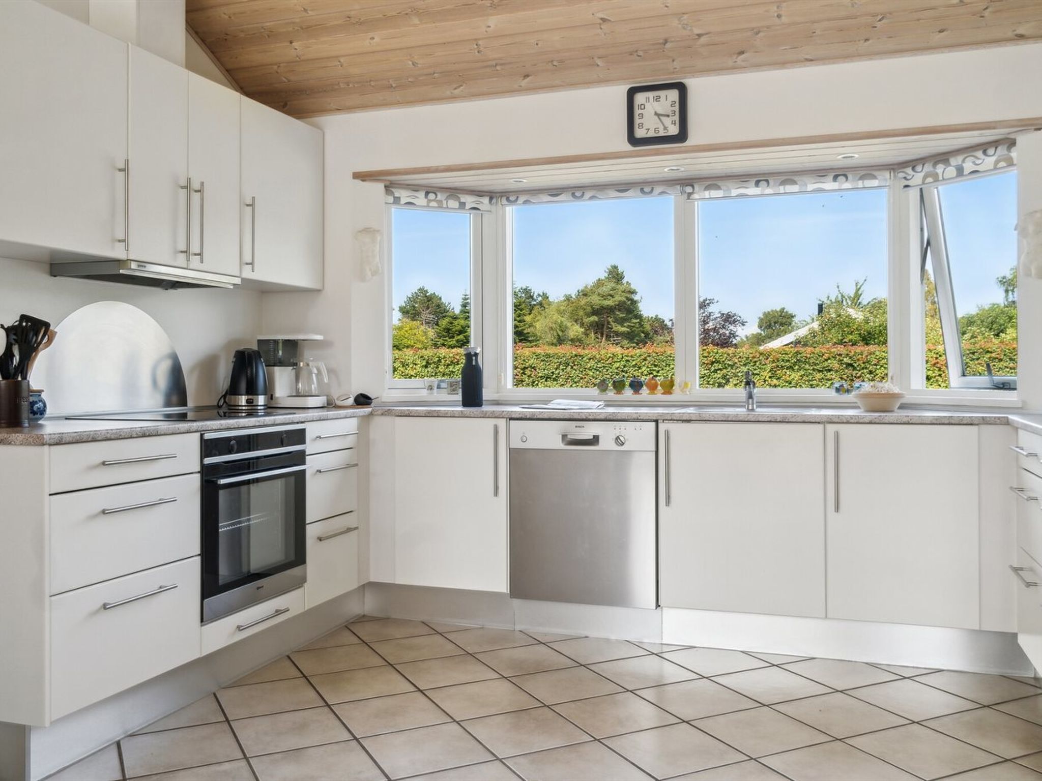 A modern kitchen with white cabinets, stainless steel appliances, and a view of greenery outside.