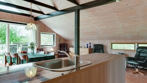 Une cuisine moderne dotée d’un grand îlot central, de poutres en bois au plafond et offrant une vue sur l’extérieur.