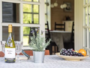 Une bouteille de vin Casillero del Diablo, une plante en pot, une assiette de raisins et une orange sur une table.