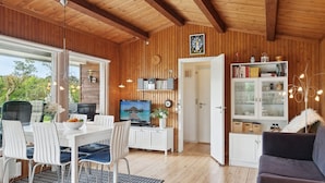 Een modern interieur met een houten plafond, een eethoek met witte stoelen en een tafel, een televisie en een boekenplank.