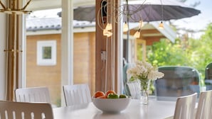 Een eetruimte met een witte tafel, stoelen, een schaal fruit en hangende hanglampen.