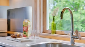 Een keuken met een roestvrijstalen spoelbak, een raam met uitzicht op groen, een groene glazen fles met bloemen en een pak appelsap.