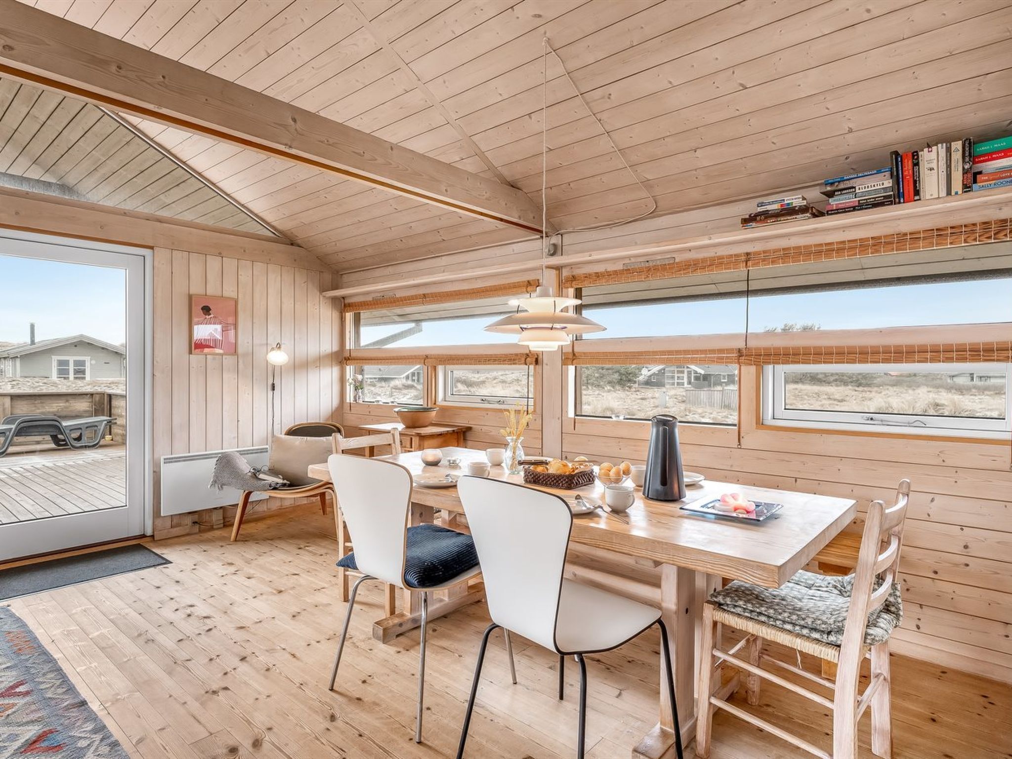 Een knus houten chalet interieur met een eethoek, grote ramen en uitzicht op buiten.