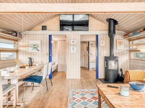 A cozy cabin interior with a dining area, a kitchen, and a living space featuring a wood-paneled ceiling and a black wood stove.