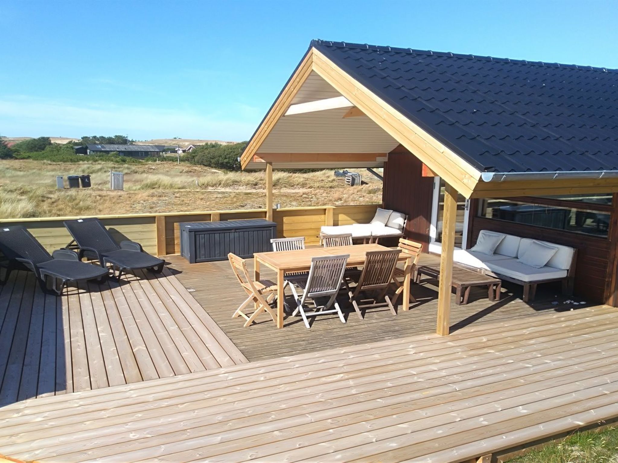 A wooden deck with a covered seating area, including a table and chairs, and a sofa.