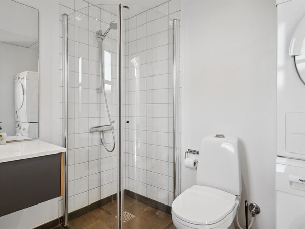 Ein modernes Badezimmer mit einer gläsernen Duschkabine, einer weißen Toilette und einem Waschbecken mit Spiegel.