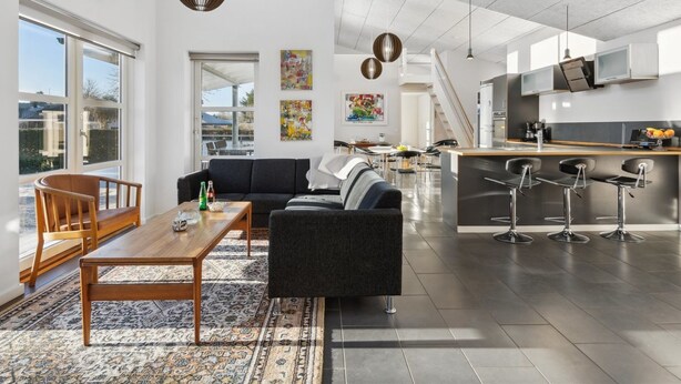 A spacious living area with a sofa, a coffee table, and a rug. There is a kitchen area with a refrigerator, a sink, and bar stools. - "Bjerne" - 200m from the sea by Interhome (Rødvig Stevns)
