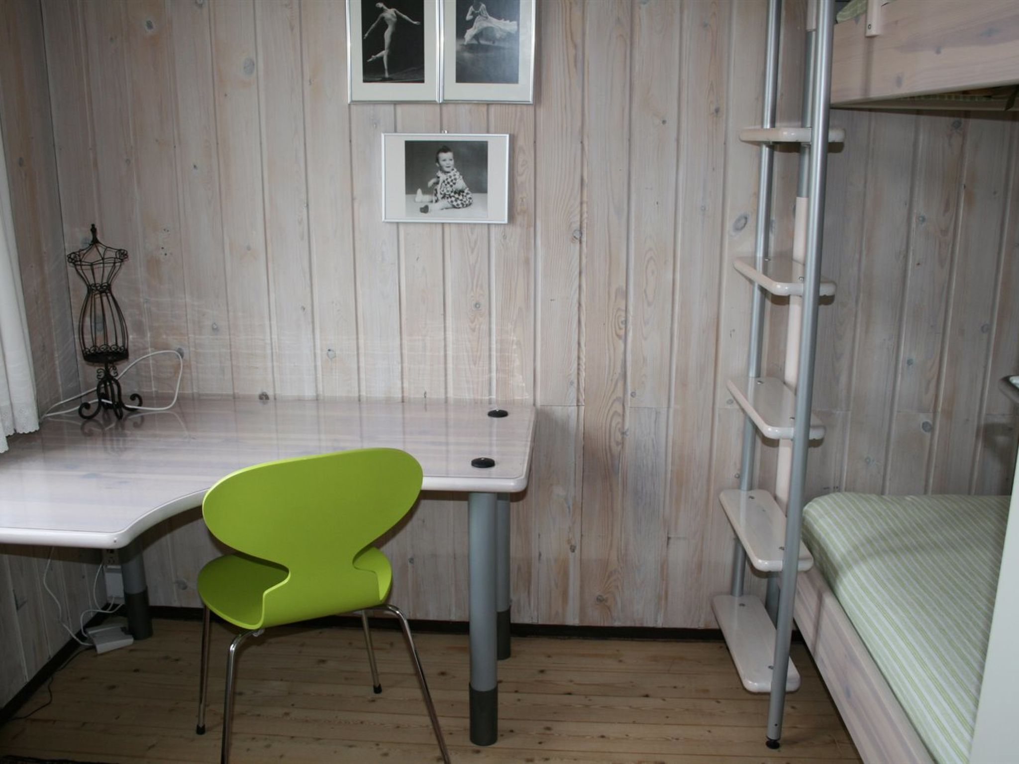 A room with a bunk bed, a desk with a chair, a small shelf, and a picture frame on the wall.
