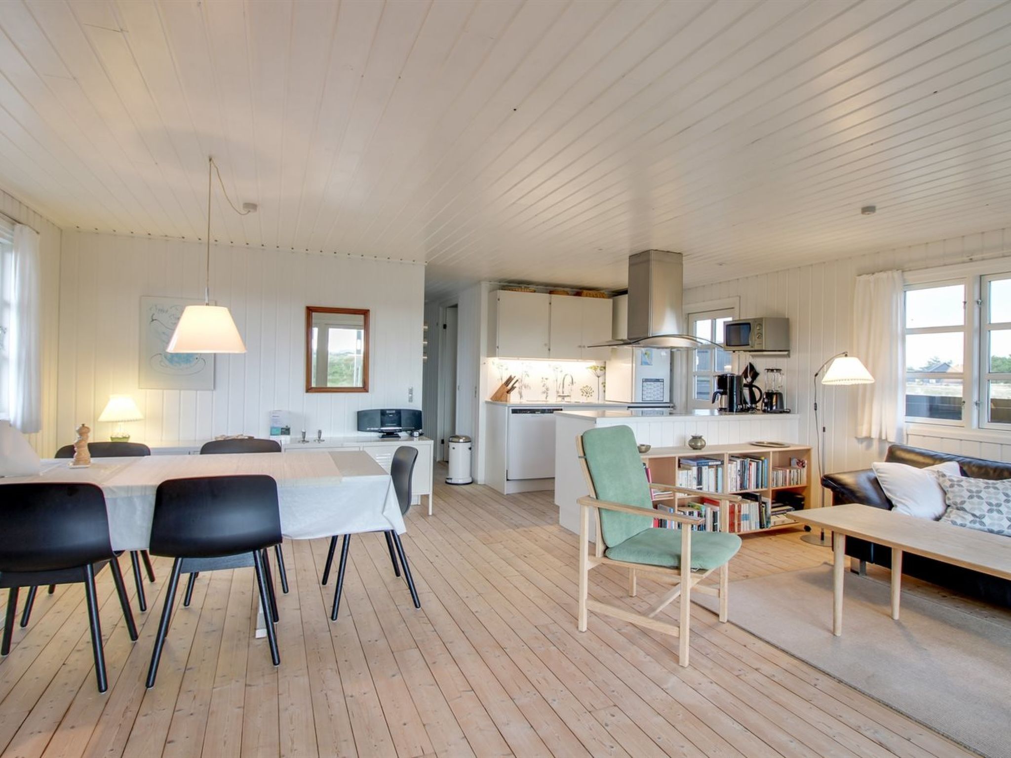 Tilava olohuone, jossa on ruokapöytä, tuoleja, sohva ja taustalla keittiö.
