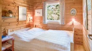 A wooden cabin room with a bed, a window with curtains, a wall-mounted lamp, and a framed picture. - "Byrge" - 2km from the sea by Interhome (Fanø)