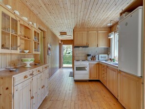 A wooden kitchen with cabinets, a stove, a microwave, and a refrigerator. - "Hege" - 450m from the sea by Interhome (Faxe Ladeplads)