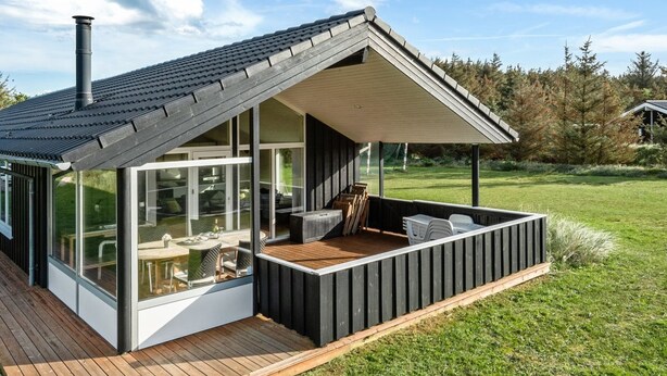 A modern house with a large glass window, a wooden deck, and a covered outdoor seating area.