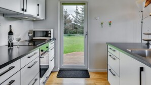 A modern kitchen with white cabinets, a black countertop, and a wooden floor. There is a window with a view of a green landscape.