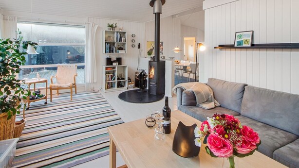 A modern living room with a fireplace, a sofa, a dining area, and a bookshelf. - "Fenneke" - 50m from the sea by Interhome (Blokhus)