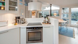 A modern kitchen with white cabinetry, a built-in oven, and a dining area with a table and chairs. - "Fenneke" - 50m from the sea by Interhome (Blokhus)