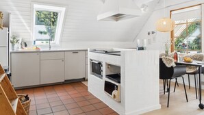 Une cuisine moderne avec des meubles blancs, une grande fenêtre et un coin repas avec des chaises noires.