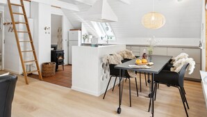 Une cuisine moderne avec des meubles blancs, un îlot central et un coin repas doté de chaises noires.