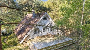Une cabane en bois blanche, dotée d’un toit à forte pente, entourée d’une forêt dense.