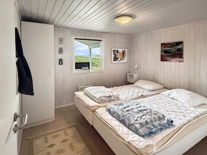 Une chambre avec deux lits, une fenêtre donnant sur un paysage verdoyant et une porte sur laquelle est accroché un manteau.