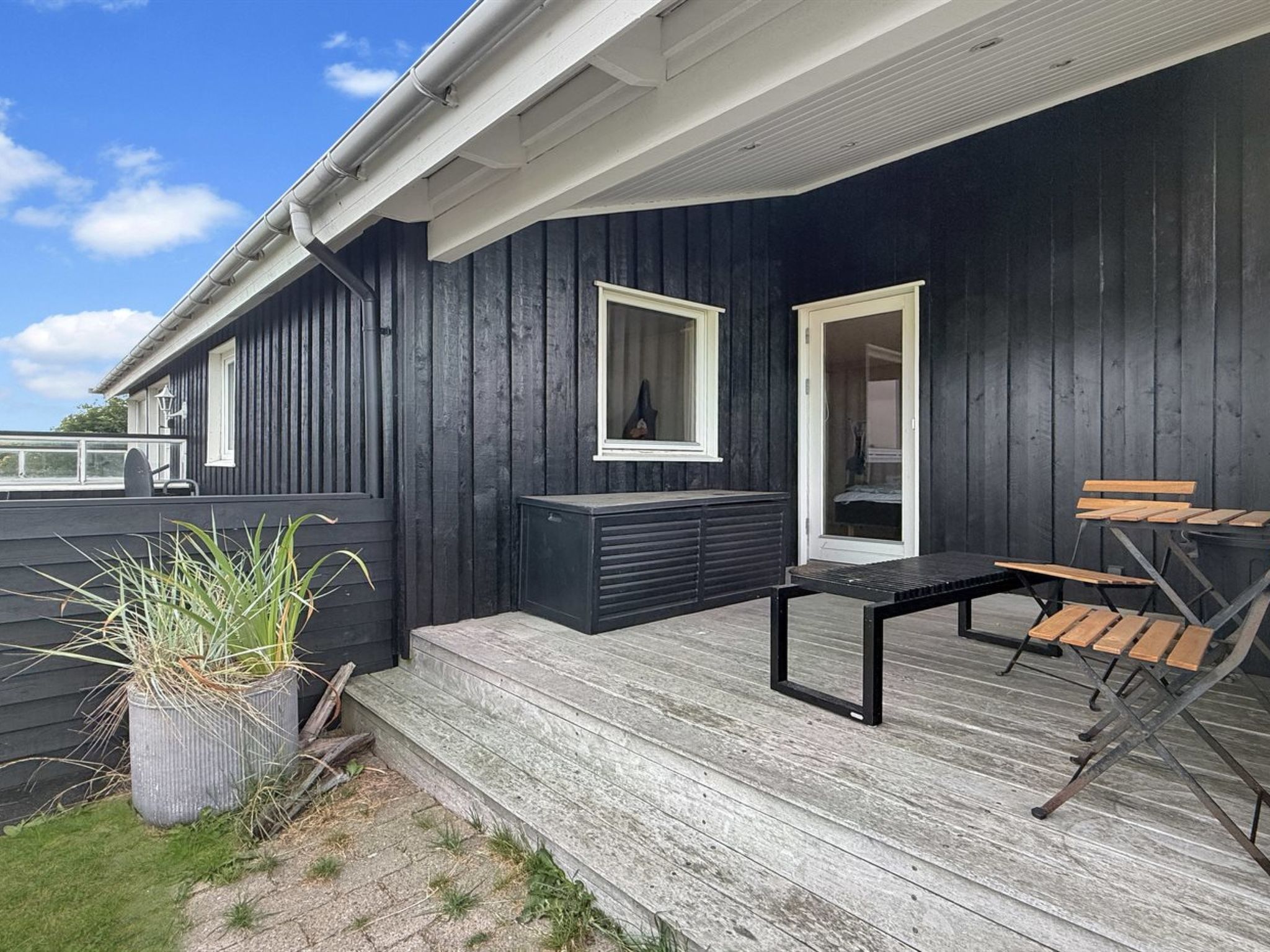 A dark wooden deck with a bench and a table, a potted plant, and a door leading to an interior space.