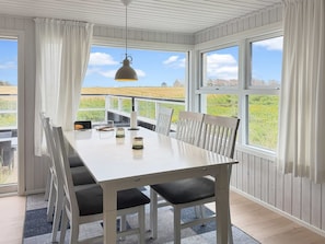 A dining area with a white table and chairs, a hanging light fixture, and large windows with curtains. - "Steffenie" - 400m from the sea by Interhome (Løkken)