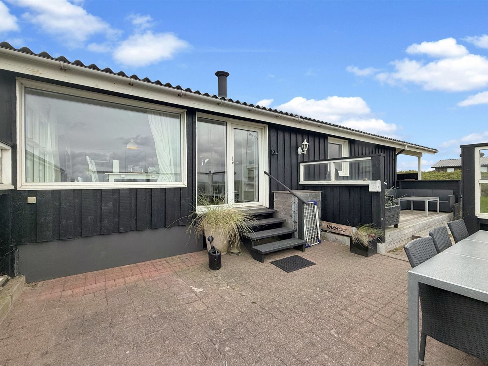 A modern house with a large window, a staircase leading to the entrance, and a patio area with outdoor furniture.