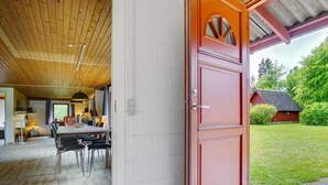 Un interior moderno con techo de madera, una zona de comedor con mesa y sillas, y una puerta roja que da al exterior.