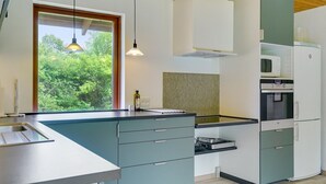 Una cocina moderna con un ventanal grande, electrodomésticos integrados y techo de madera.