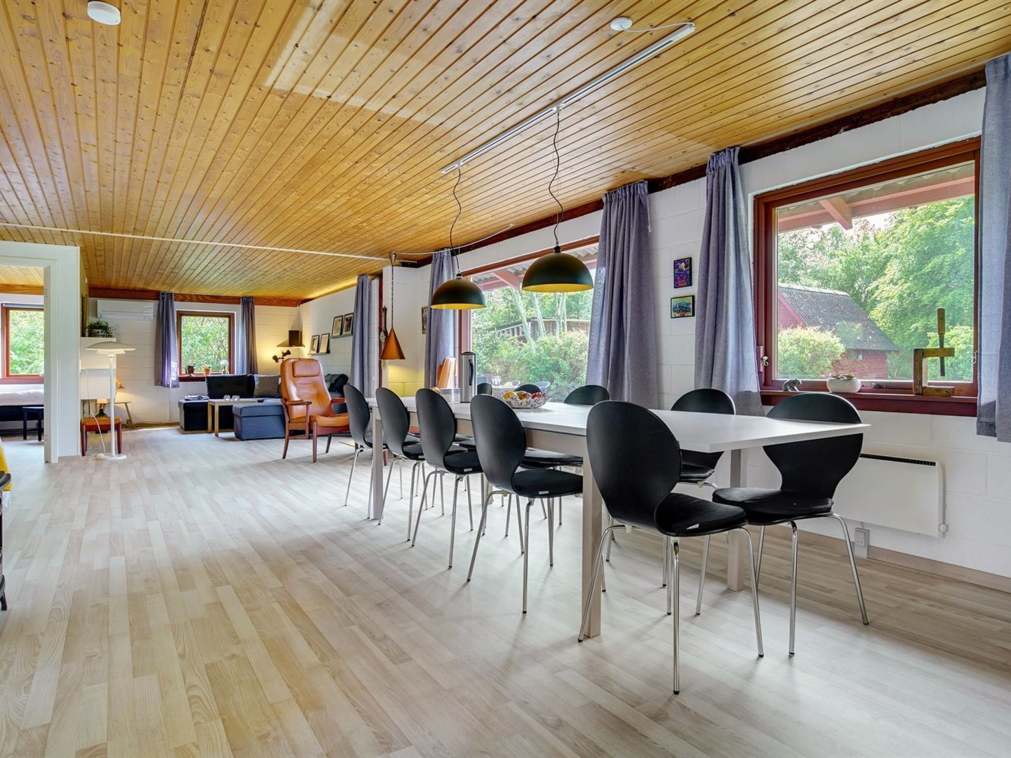 Un comedor amplio con una mesa larga y varias sillas, suelo de madera y ventanas grandes con cortinas.
