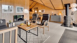 A cozy cabin interior with wooden walls, a dining area, a living room with a TV, and a wood stove. - "Ija" - 200m from the sea by Interhome (Føllenslev)