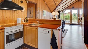 A modern kitchen with wooden walls and a large window, a stove, and a dishwasher. - "Ija" - 200m from the sea by Interhome (Føllenslev)