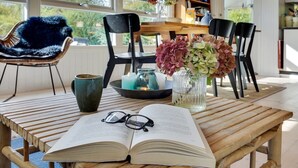 A wooden table with an open book and glasses, a blue chair, and a vase with flowers. - "Gærmund" - 350m from the sea by Interhome (Føllenslev)