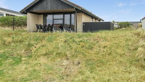 Et moderne hus med skråt tag, store vinduer og en overdækket terrasse med stole.