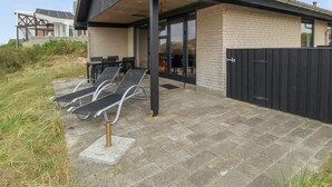 En moderne bygning med en overdækket terrasse, udendørs siddepladser og udsigt over det omkringliggende landskab.